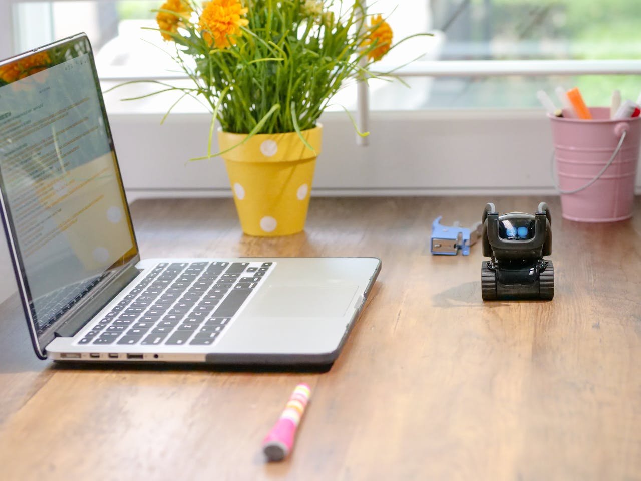 Stylish workspace featuring a laptop, toy robot, and vibrant flowers in natural light.